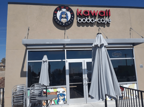 Exterior of Kawafi Boba Cafe with a sign, open umbrellas, and chairs stacked outside on a sunny day.